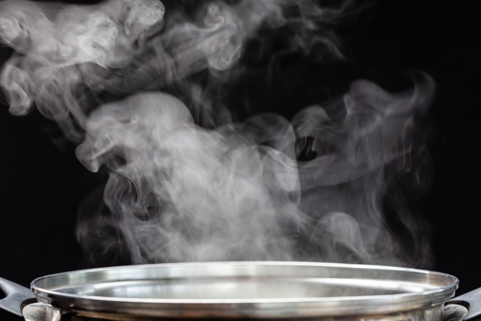 Traditional silver cooking pot with white smoke while cooking on black background